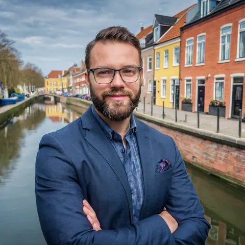A man in a blue suit stands by a canal with colorful buildings in the background.