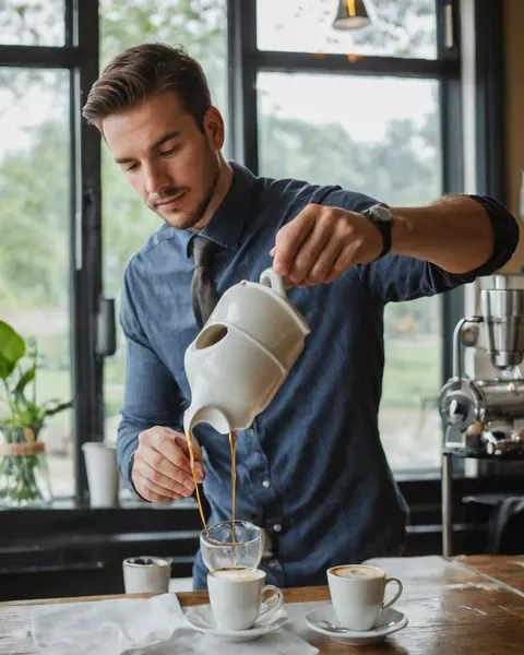 Barista pouring espresso into a glass cup at a cafe counter near a window