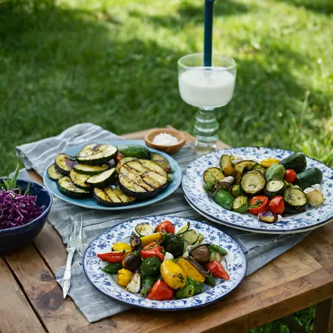Three plates of grilled vegetables and purple cabbage salad on a wooden table outdoors.